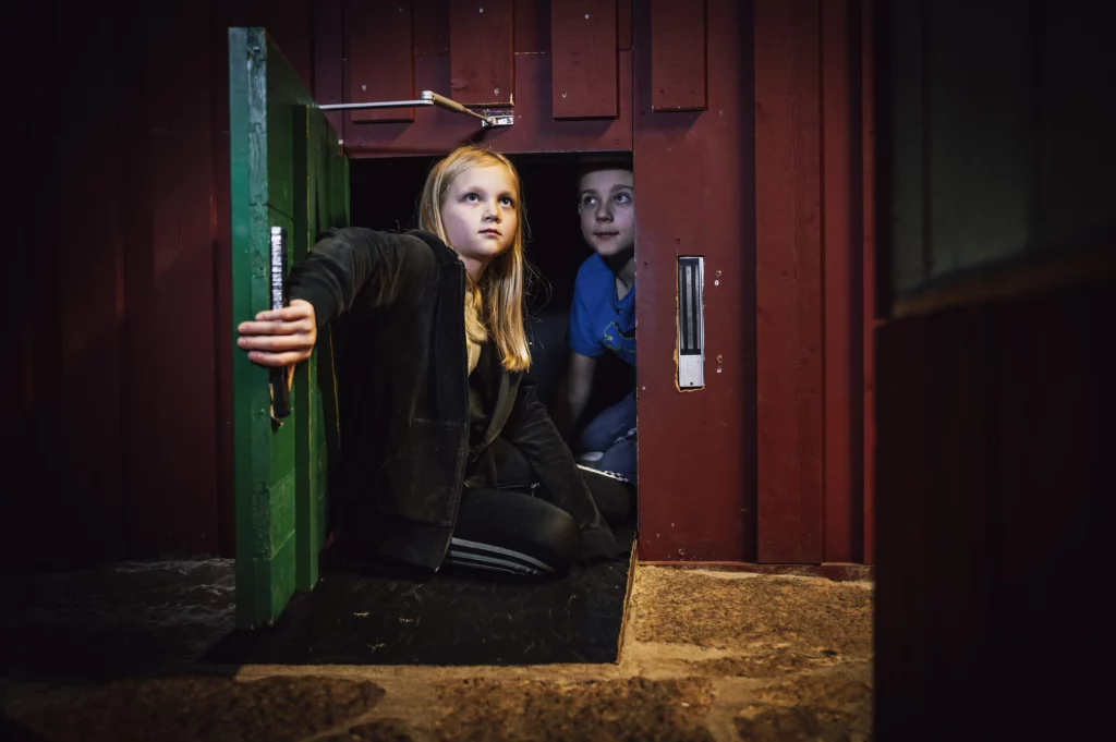 En flicka och en pojke kommer ut ur en lucka i väggen