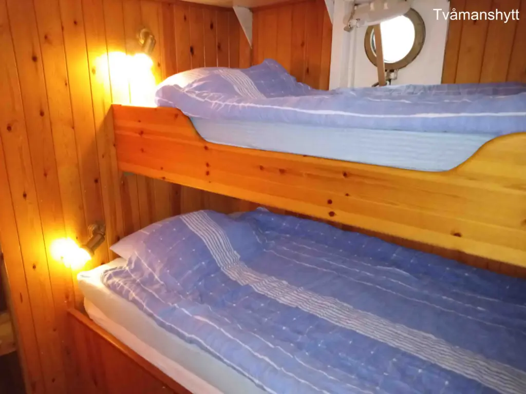 en liten hytt med två sängar och ett runt litet fönster