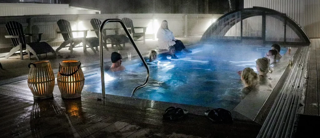 varm pool utomhus där en grupp vuxna badar på kvällen.