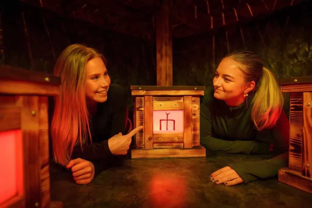 två tjejer ligger på golvet med en låda mellan sig. en tjej pekar på lådan