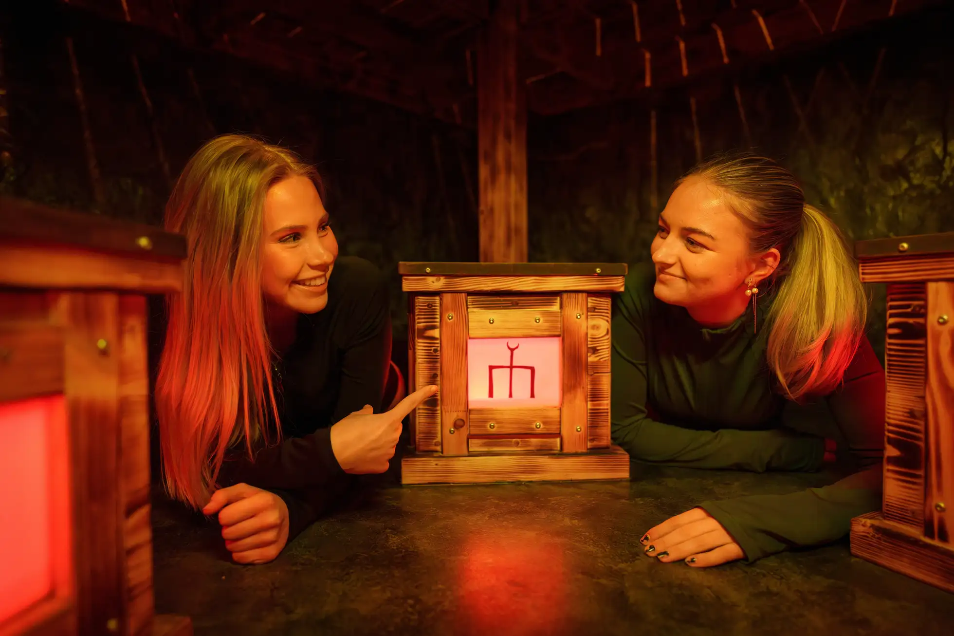 två tjejer ligger på golvet med en låda mellan sig. en tjej pekar på lådan