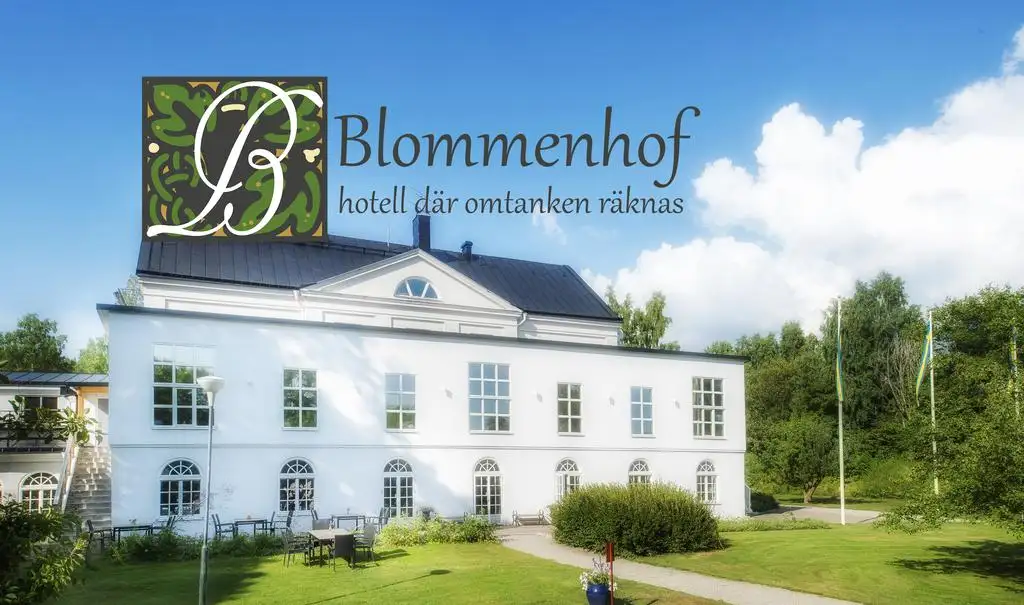 Blommenhof hotell, vit byggnad i tre våningar med stora fönster. Gröna träd, gräsmatta och skog runtom